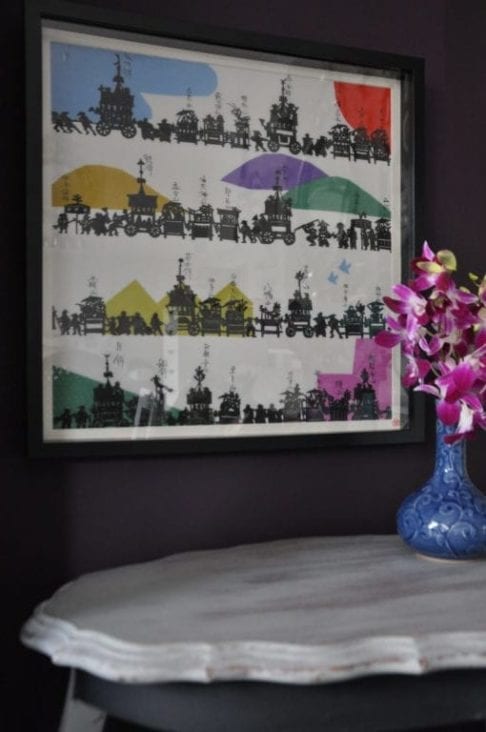 A black framed, colourful, Japanese, silkscreen print above A French side table with a vase of pink orchids.