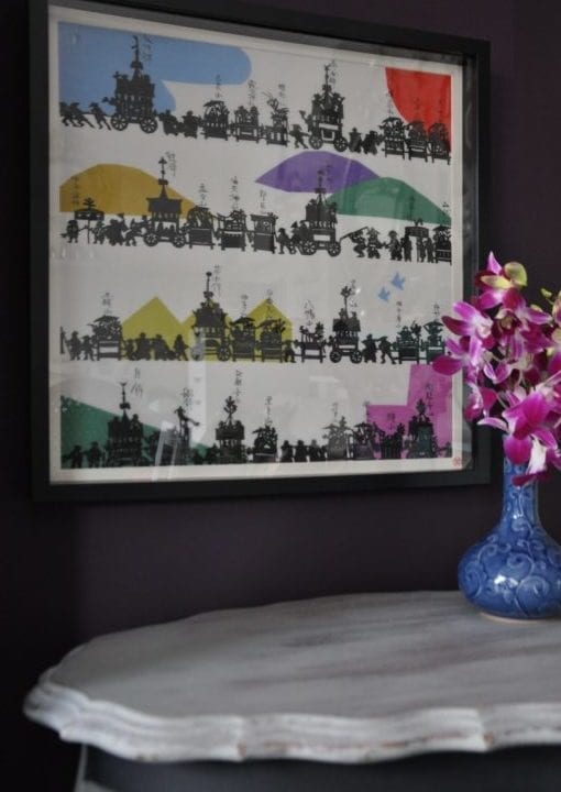 A black framed, colourful, Japanese, silkscreen print above A French side table with a vase of pink orchids.