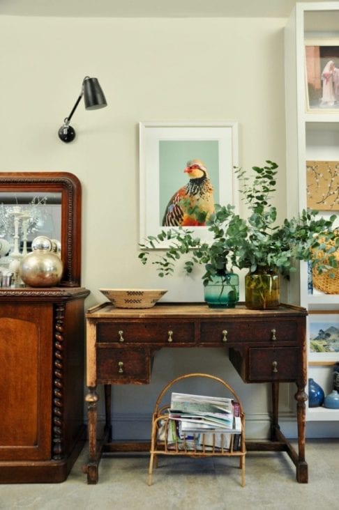 A giclée digital art print of a partridge above a mahogany desk and vase with eucalyptus.