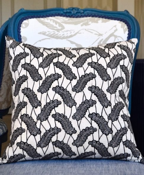 A chic black and white botanical cushion in African Dutch wax print fabric on a blue French chair.