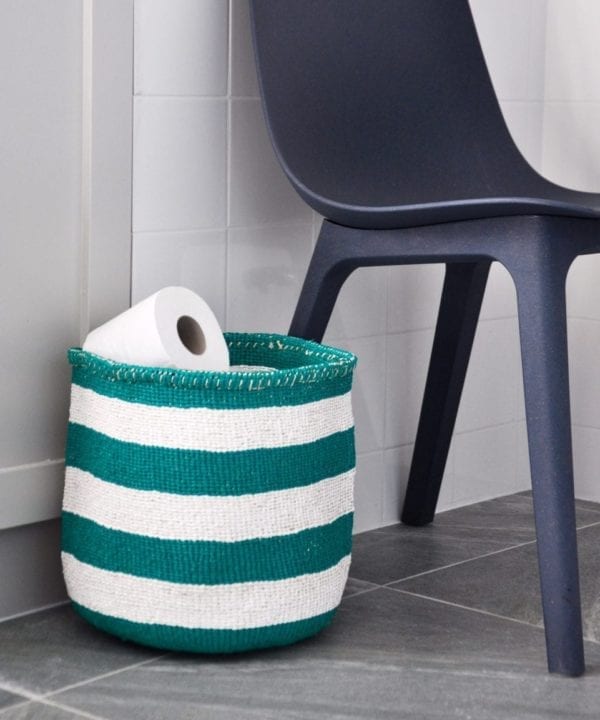 A jade green striped basket used as a loo roll holder with a chair in the background.