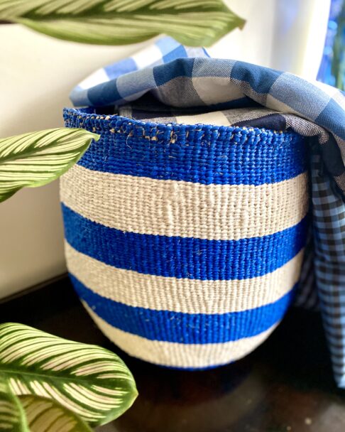 A blue and white striped, stylish storage basket with leaves in the foreground.