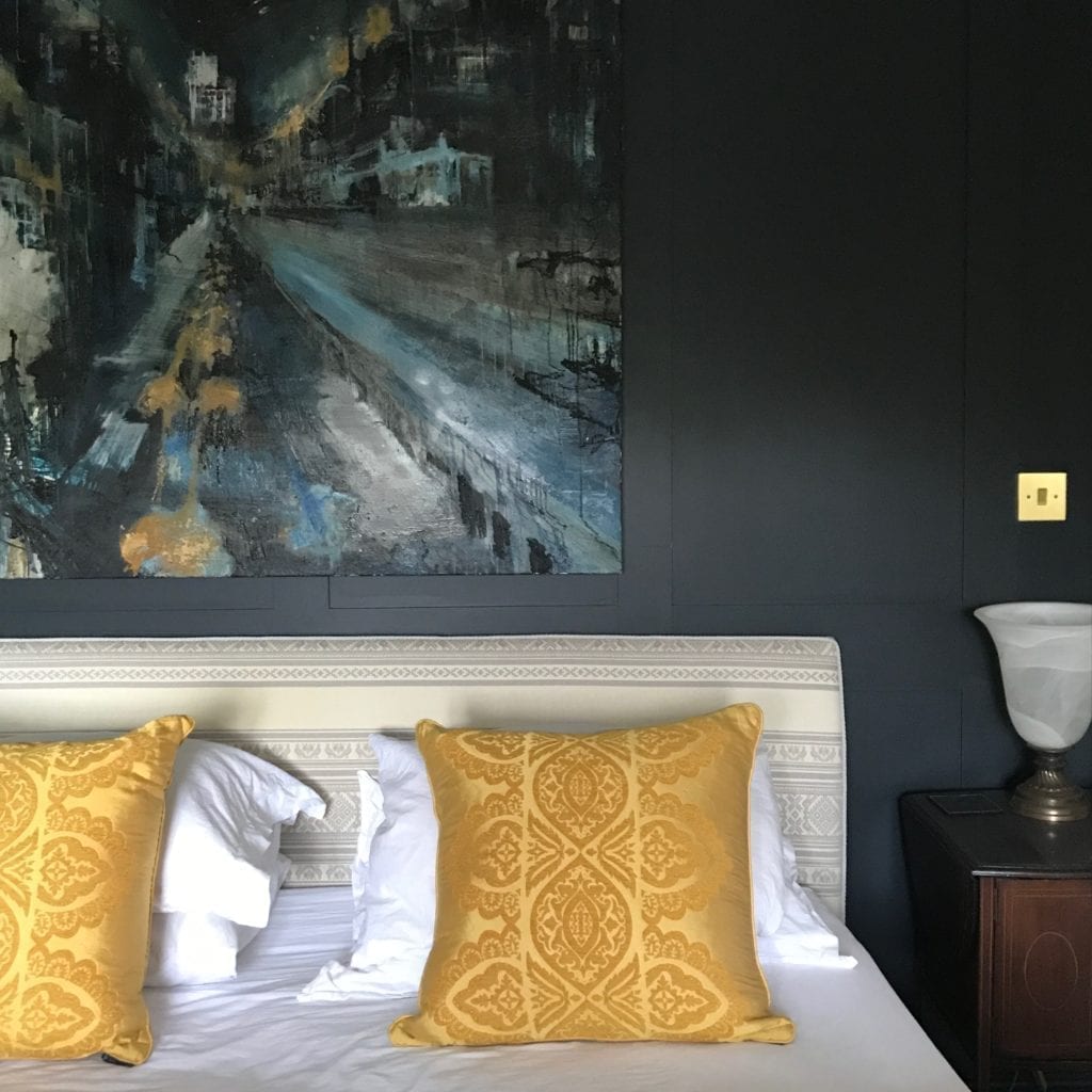 An elegant bedroom with dark walls and saffron yellow silk cushions on a bed at the home of textile designer, Julia Brendel.