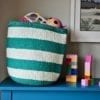 Striped toy storage baskets in jade and white, woven and handmade in Kenya. Filled with colourful kids toys.