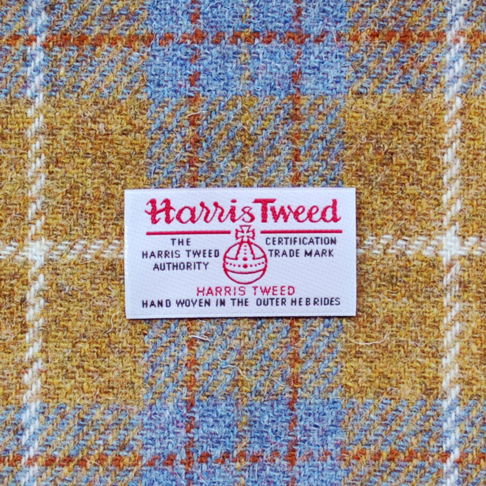 A close-up shot of the Harris Tweed Authority orb label of authenticity against a grey and mustard drum shade.