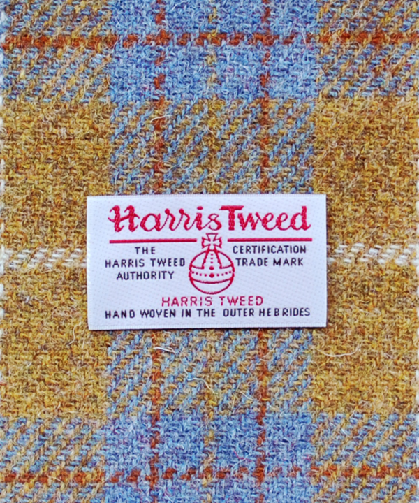 A close-up shot of the Harris Tweed Authority orb label of authenticity against a grey and mustard drum shade.