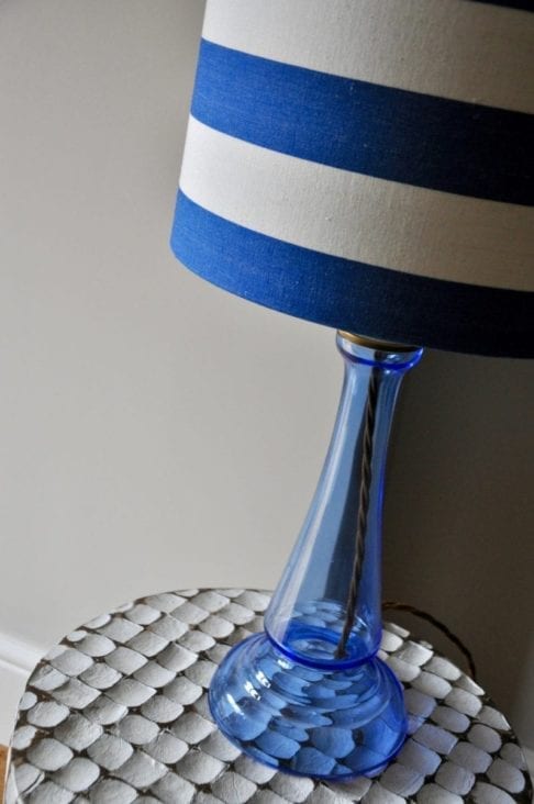 A blue glass base with a blue and white striped lamp base on a carved, white, wooden side table.