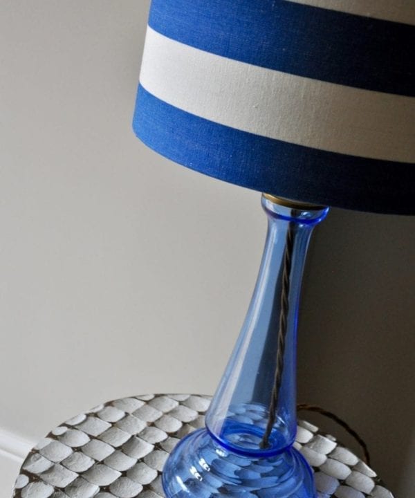 A blue glass base with a blue and white striped lamp base on a carved, white, wooden side table.