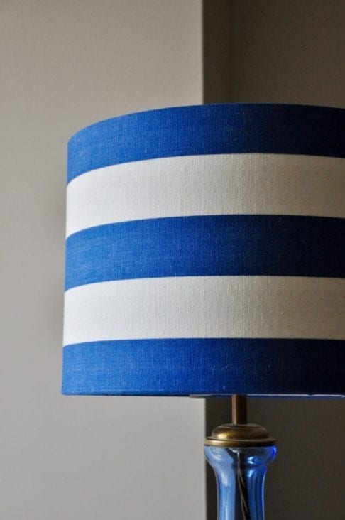 A blue and white stripe drum lampshade on a blue glass base.