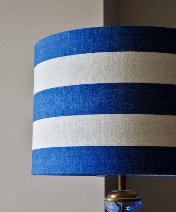 A blue and white stripe drum lampshade on a blue glass base.