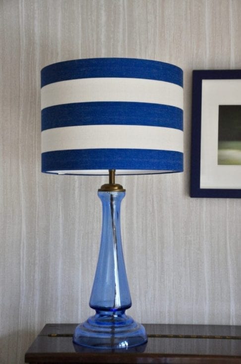 A Royal blue striped lampshade on a blue glass lamp base against a pale backdrop.