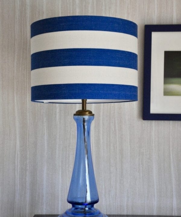 A Royal blue striped lampshade on a blue glass lamp base against a pale backdrop.