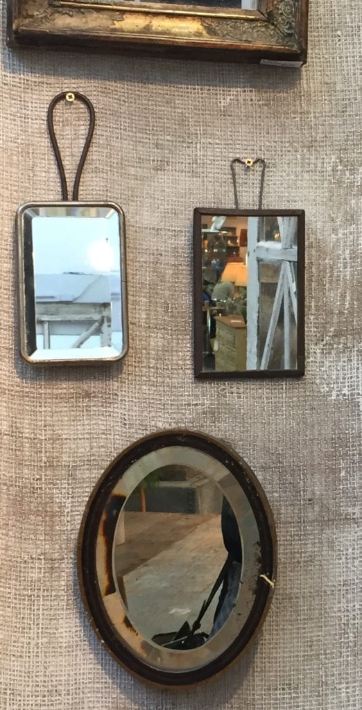 A collection of small vintage mirrors displayed on a hessian-clad wall.