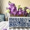 The Dutch, Delft-pottery-inspired 'Flowerbrick' rectangular vase on a dining table with a beige striped tablecloth and a geometric wallpaper backdrop.