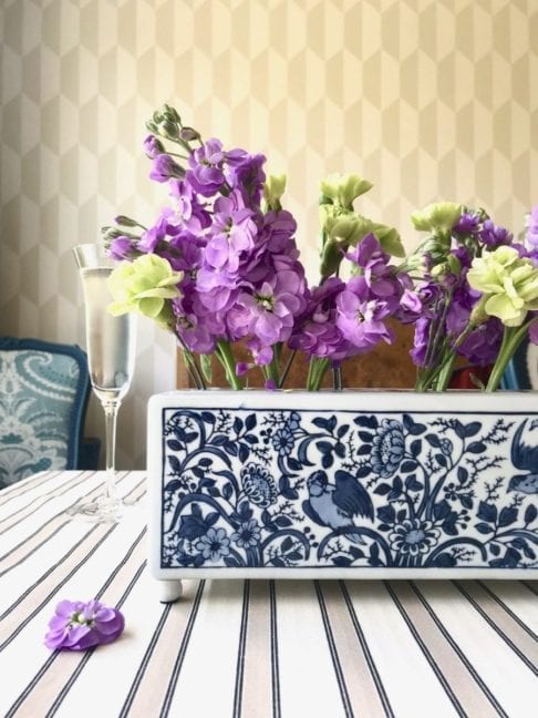 The Dutch, Delft-pottery-inspired 'Flowerbrick' rectangular vase on a dining table with a beige striped tablecloth and a geometric wallpaper backdrop.