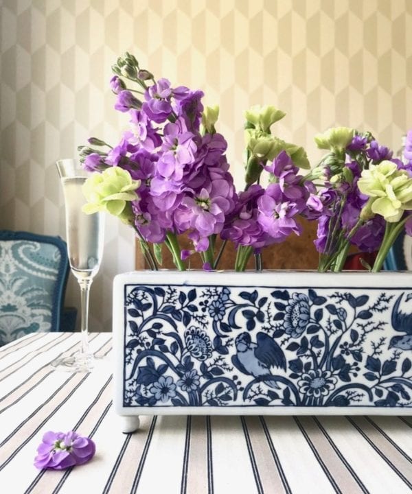 The Dutch, Delft-pottery-inspired 'Flowerbrick' rectangular vase on a dining table with a beige striped tablecloth and a geometric wallpaper backdrop.