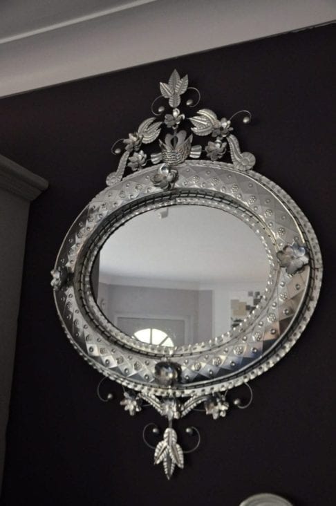 A unique, oval, hand-stamped tin, decorative, Mexican mirror hung against a dark painted wall.