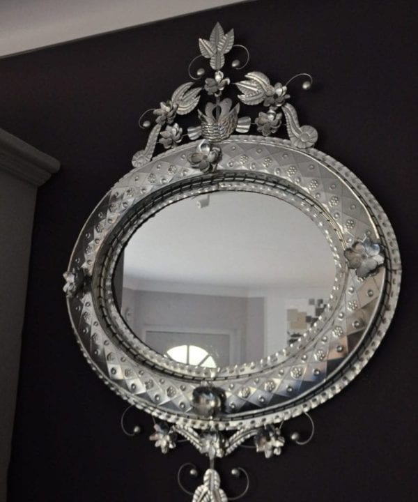 A unique, oval, hand-stamped tin, decorative, Mexican mirror hung against a dark painted wall.