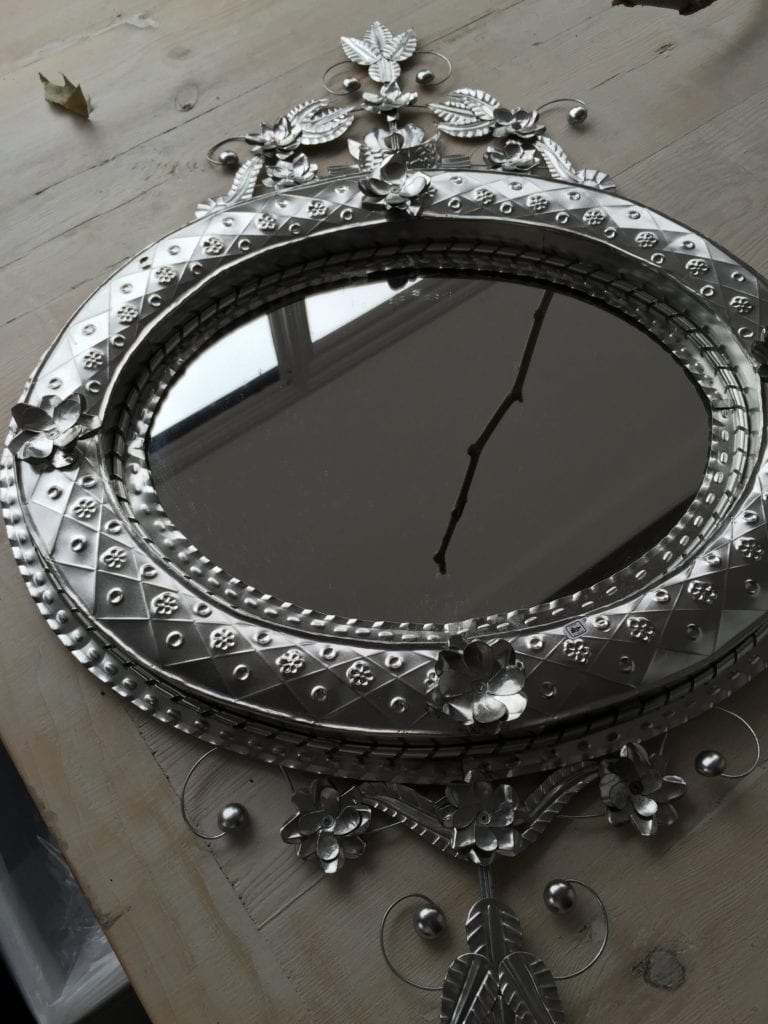 A unique, oval, hand-stamped tin, decorative, Mexican mirror laid on a table.