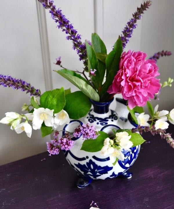 Dutch-style, Delft-blue, small vase filled with pink and purple summer blooms and displayed on a purple painted wooden surface.