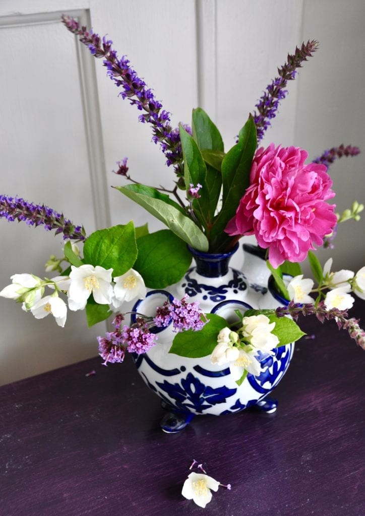 Dutch-style, Delft-blue, small vase filled with pink and purple summer blooms and displayed on a purple painted wooden surface.