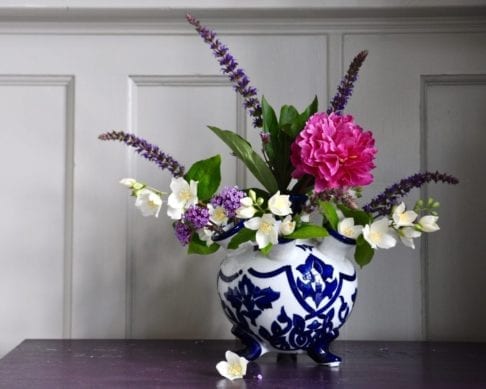 Dutch traditional style small tulip vase with pink, cream and purple summer blooms on a purple sideboard.