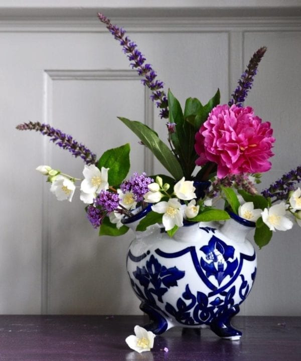 Dutch traditional style small tulip vase with pink, cream and purple summer blooms on a purple sideboard.