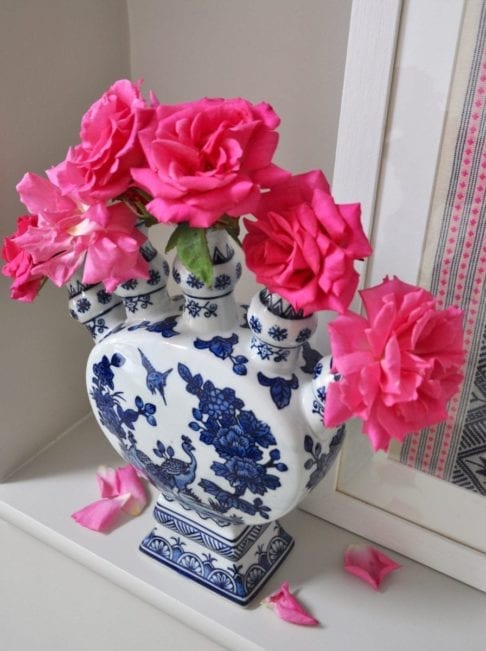 An overhead shot of a Dutch-inspired blue and white painted tulip vase filled with pink roses on a shelf.