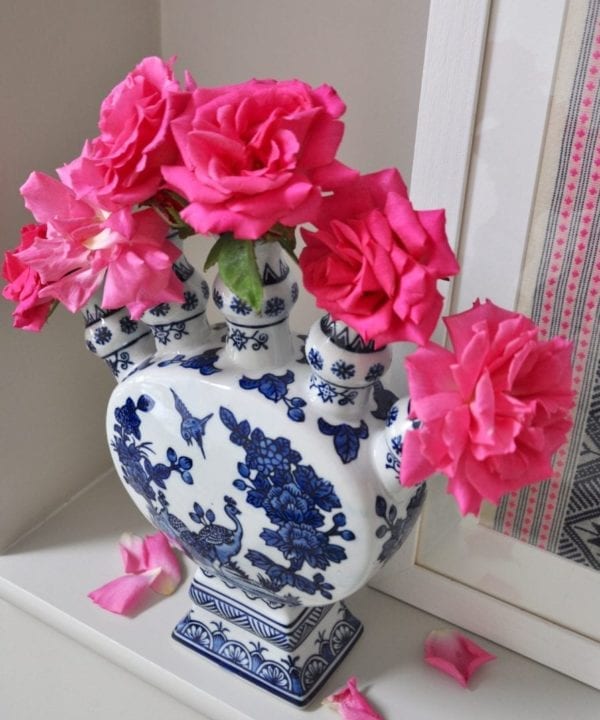 An overhead shot of a Dutch-inspired blue and white painted tulip vase filled with pink roses on a shelf.