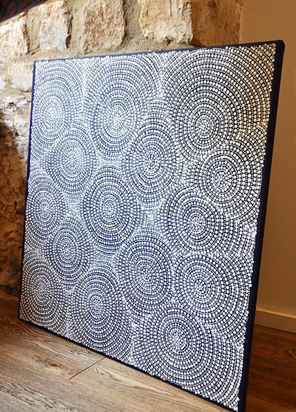 An Aboriginal art canvas depicting concentric circles created from dots in white on a blue ground.