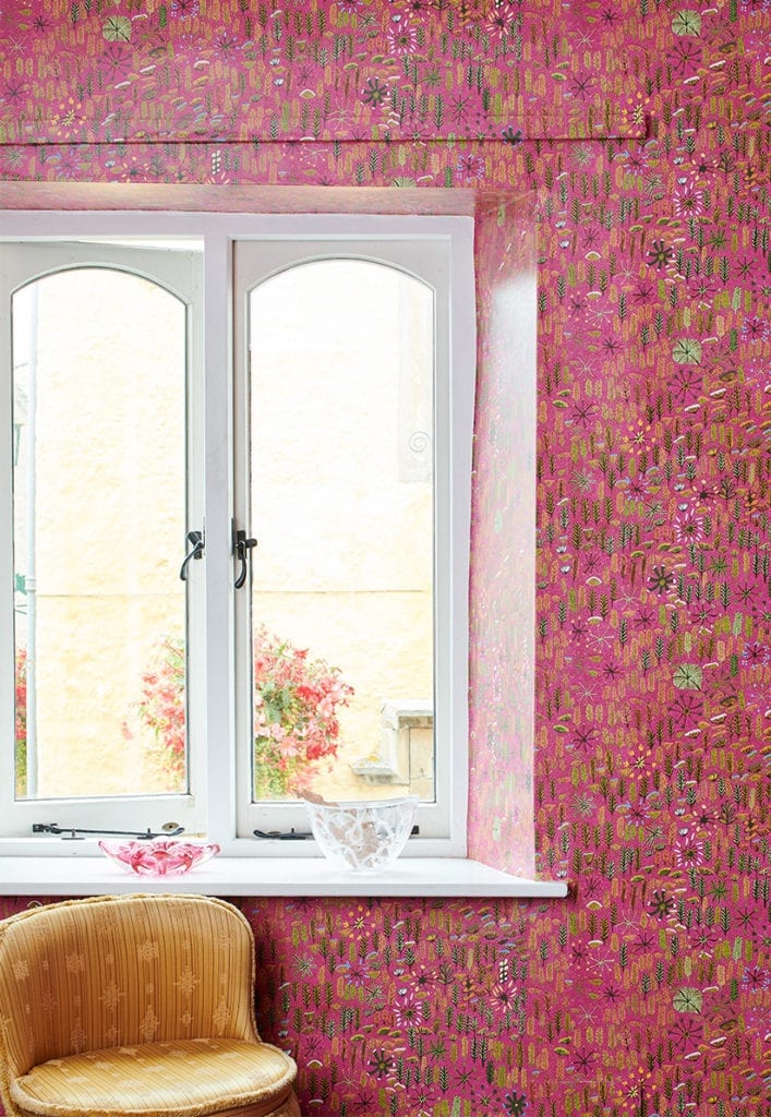 Aboriginal culture wallpaper 'Betty' in pink shown in a room setting by a window with chair in foreground.