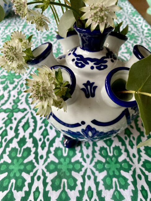 Detail of a blue and white Dutch flower vase on a patterned green tablecloth