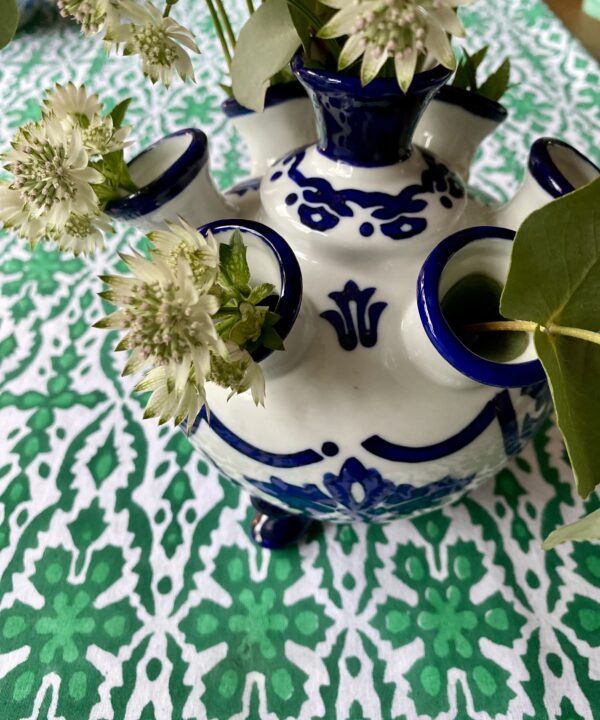 Detail of a blue and white Dutch flower vase on a patterned green tablecloth