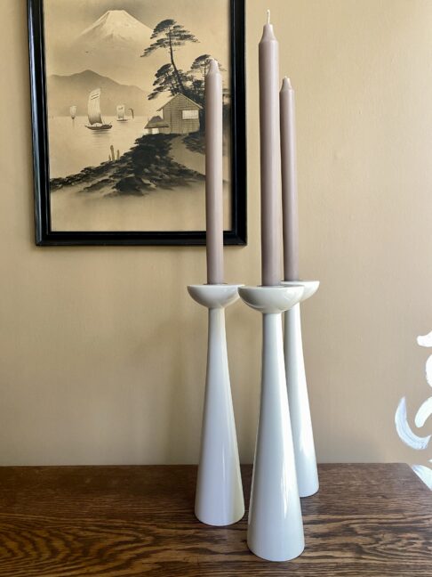 A trio of tall, white candlesticks against a neutral backdrop.