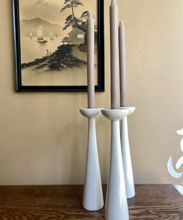 A trio of tall, white candlesticks against a neutral backdrop.