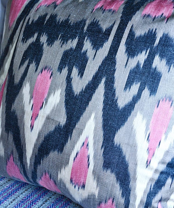 Detail of a pink and warm, grey, silk ikat cushion with black accents.