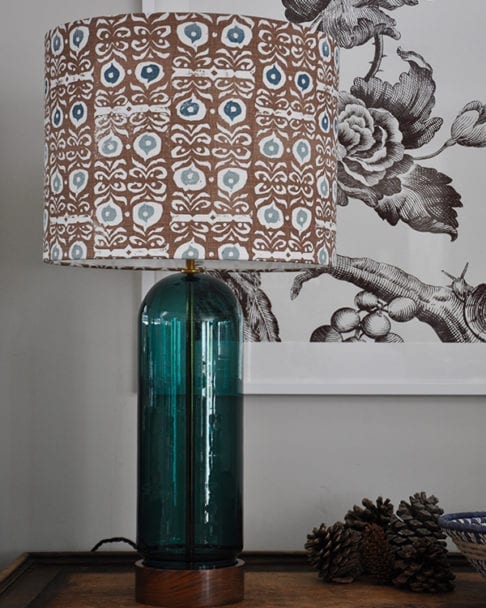 A patterned lampshade in teal blues and brown with a teal glass lampbase.