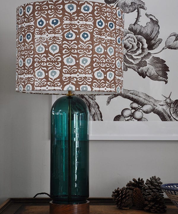 A patterned lampshade in teal blues and brown with a teal glass lampbase.