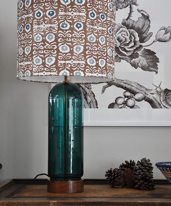 A patterned lampshade in teal blues and brown on a teal glass and wood base.