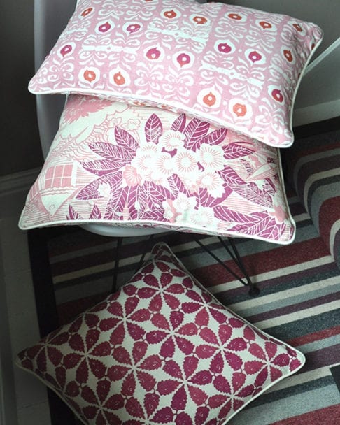 A trio of pink and raspberry cushions: Iznik, Webb's Wonder pink floral cushion and Maroc on a chair and stripy carpet. Available from Telescope Style.