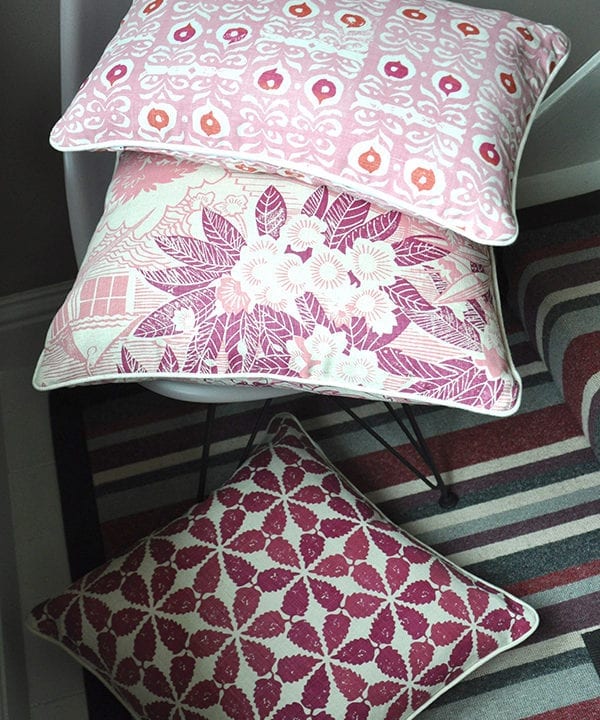 A trio of pink and raspberry cushions: Iznik, Webb's Wonder pink floral cushion and Maroc on a chair and stripy carpet. Available from Telescope Style.