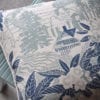 A pale blue floral cushion depicting an Arts & Crafts house in it's garden setting photographed on a pale turquoise chair.