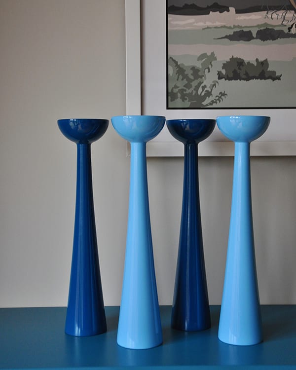 Tall coloured candlesticks in glossy blue hues sat on a teal painted sideboard.