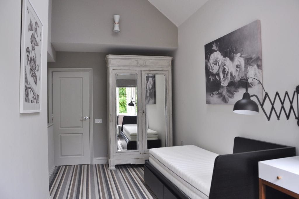 A grey room scheme featuring a French painted armoire, a day bed, a peony print and stripy, neutral carpet.