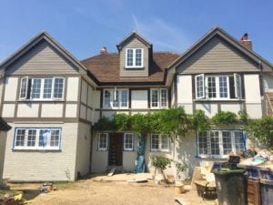 A 1930s exterior house renovation mid-project, featuring gable ends, mock-Tudor beams, painted beams and brickwork.