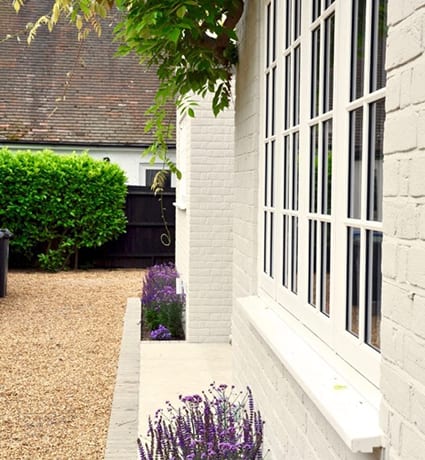 Painted brickwork house exterior in cream with purple planting.