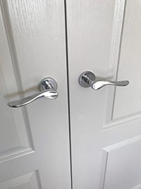 A pair of curved chrome interior door handles on painted double doors.