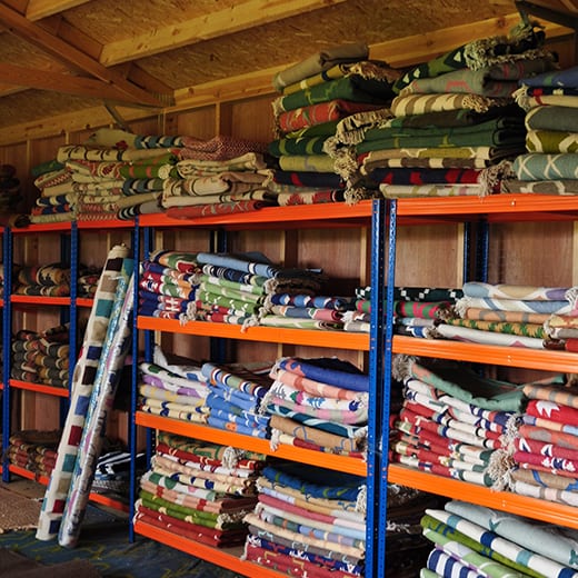 Rows of shelving piled up with colourful dhurrie rug designs available from Mahout Lifestyle at their north Oxfordshire base.