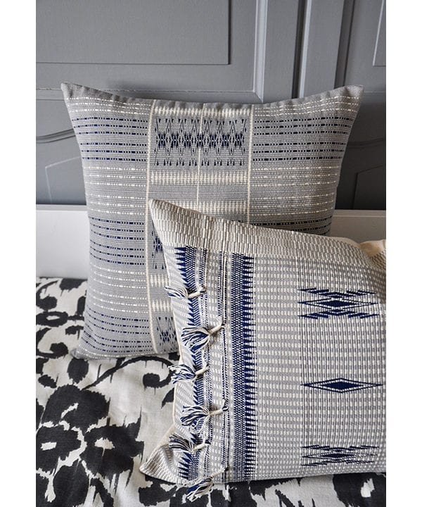 Tasselled blue grey cushion covers handmade in Nagaland, India against grey panelling.