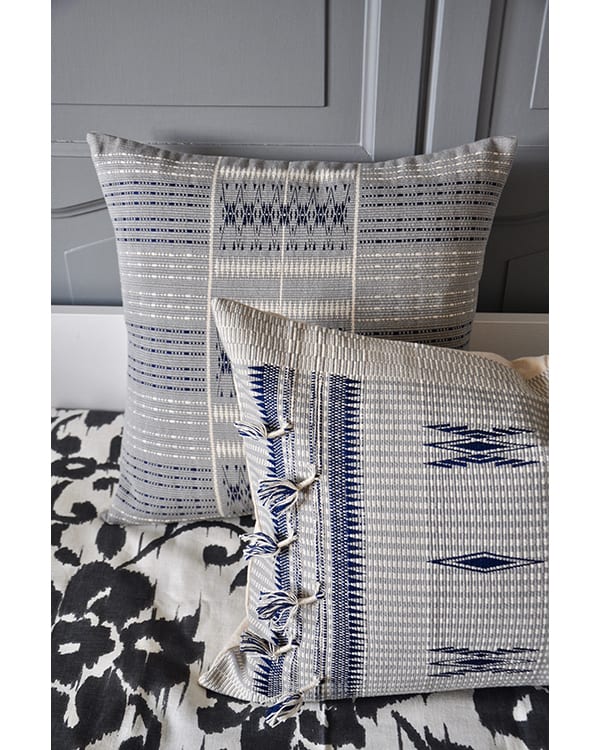 Tasselled blue grey cushion covers handmade in Nagaland, India against grey panelling.